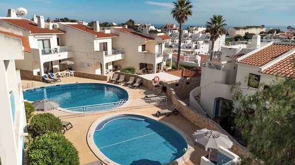 A rooftop swimming pool with lounge chairs and umbrellas, surrounded by white buildings with red-tiled roofs and palm trees. - Monte Dourado Resort (Lagoa)