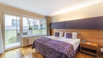 Quarto de hotel com uma cama grande, cabeceira de madeira, mesa de cabeceira com telefone e vista para a varanda.