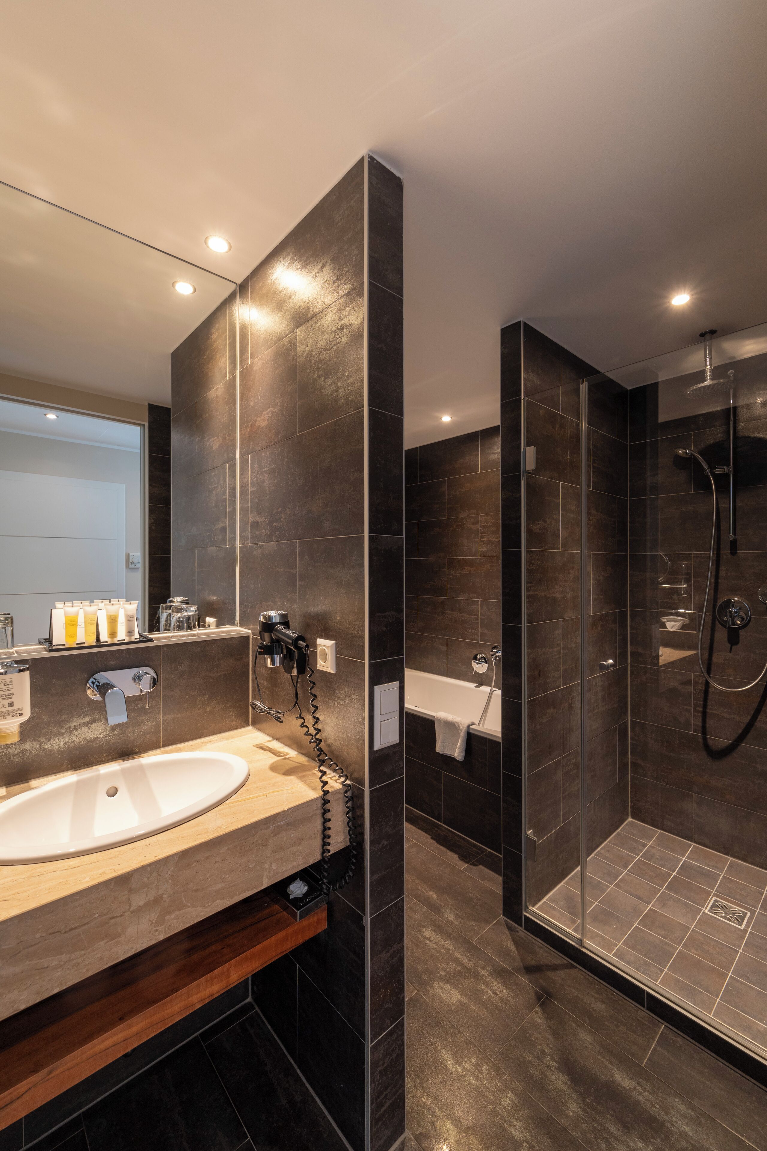 A modern bathroom with a large sink, a glass-enclosed shower, and dark tiled walls.
