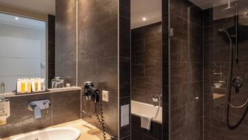 A modern bathroom with a large sink, a glass-enclosed shower, and dark tiled walls.