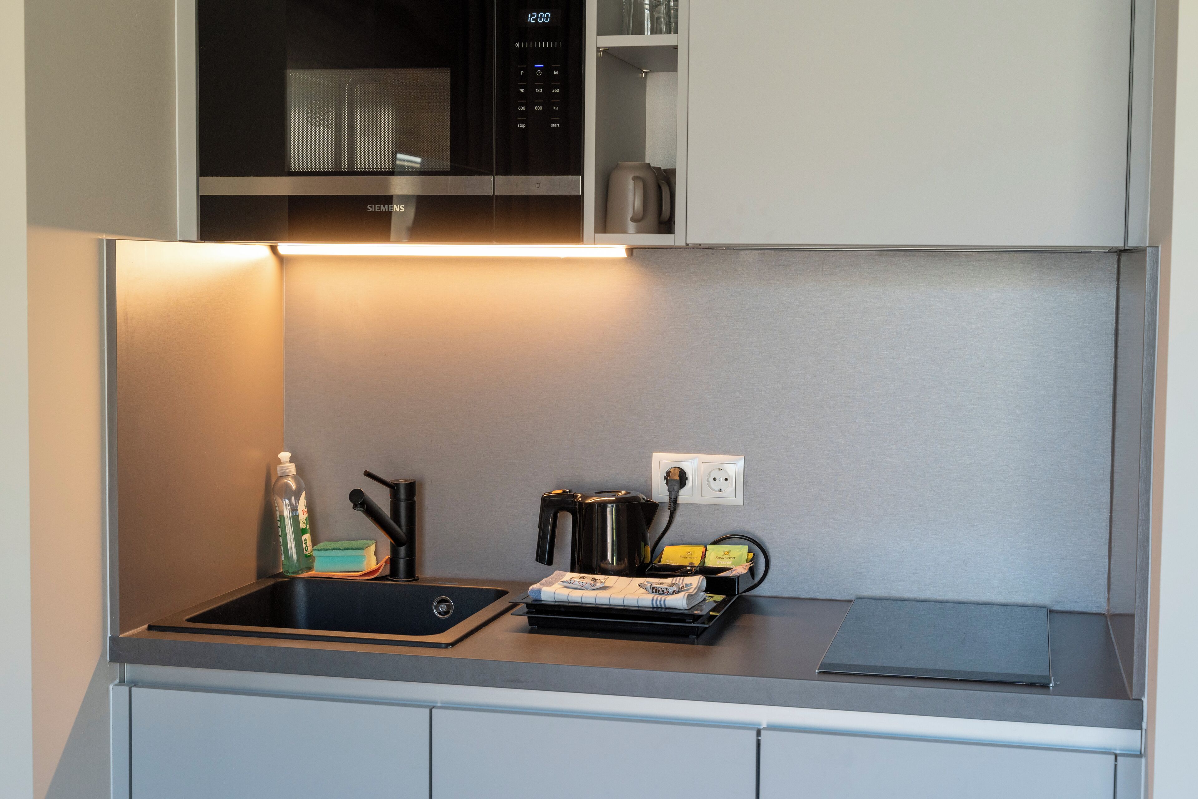Una cocina compacta con microondas, hervidor y cafetera sobre la encimera.