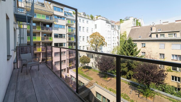A balcony with a chair, a view of neighboring buildings, and a clear sky. - Pakat Suites (Vienna)
