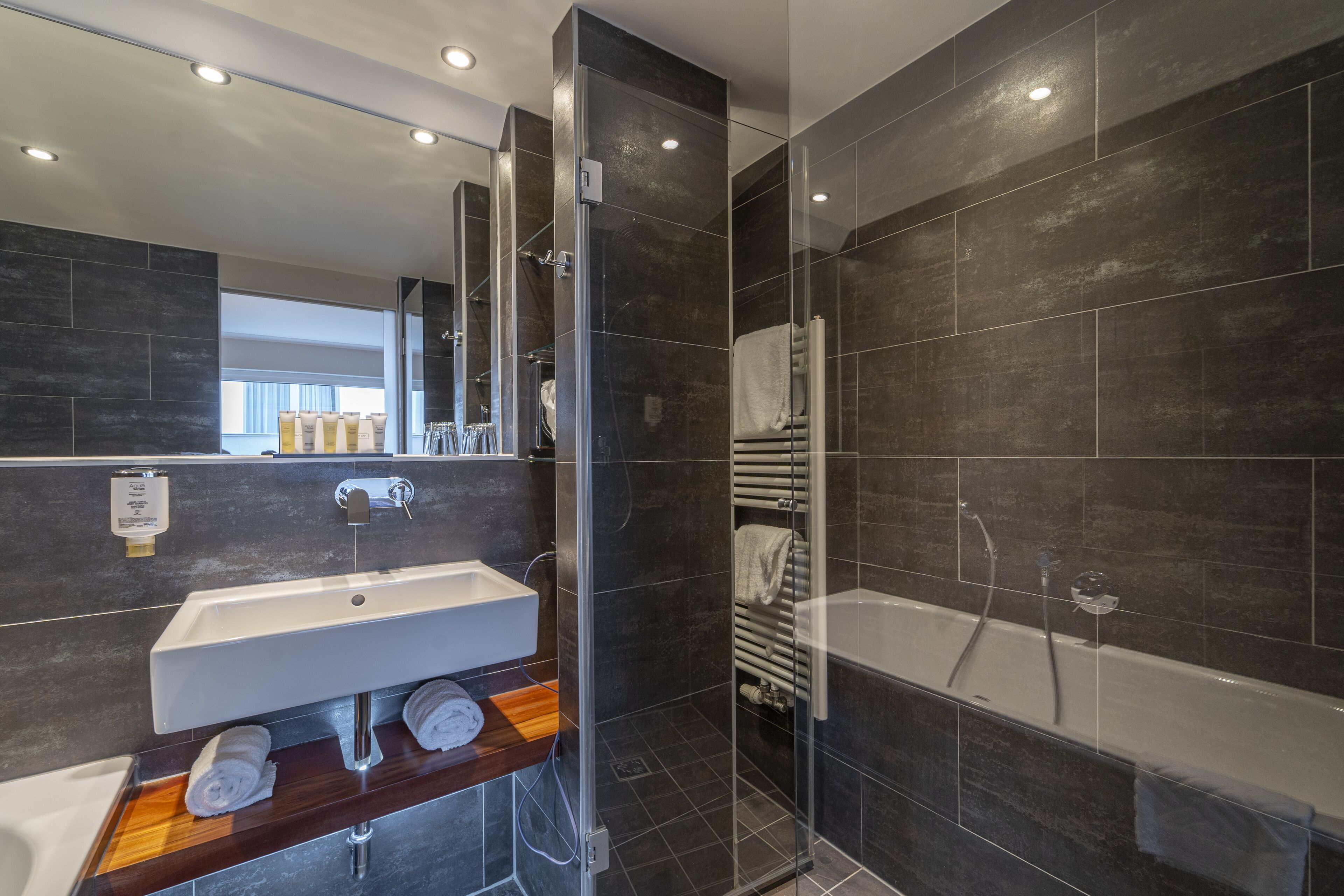 Een moderne badkamer met een douchecabine van glas, een wit wastafelmeubel en een houten opbergkast.
