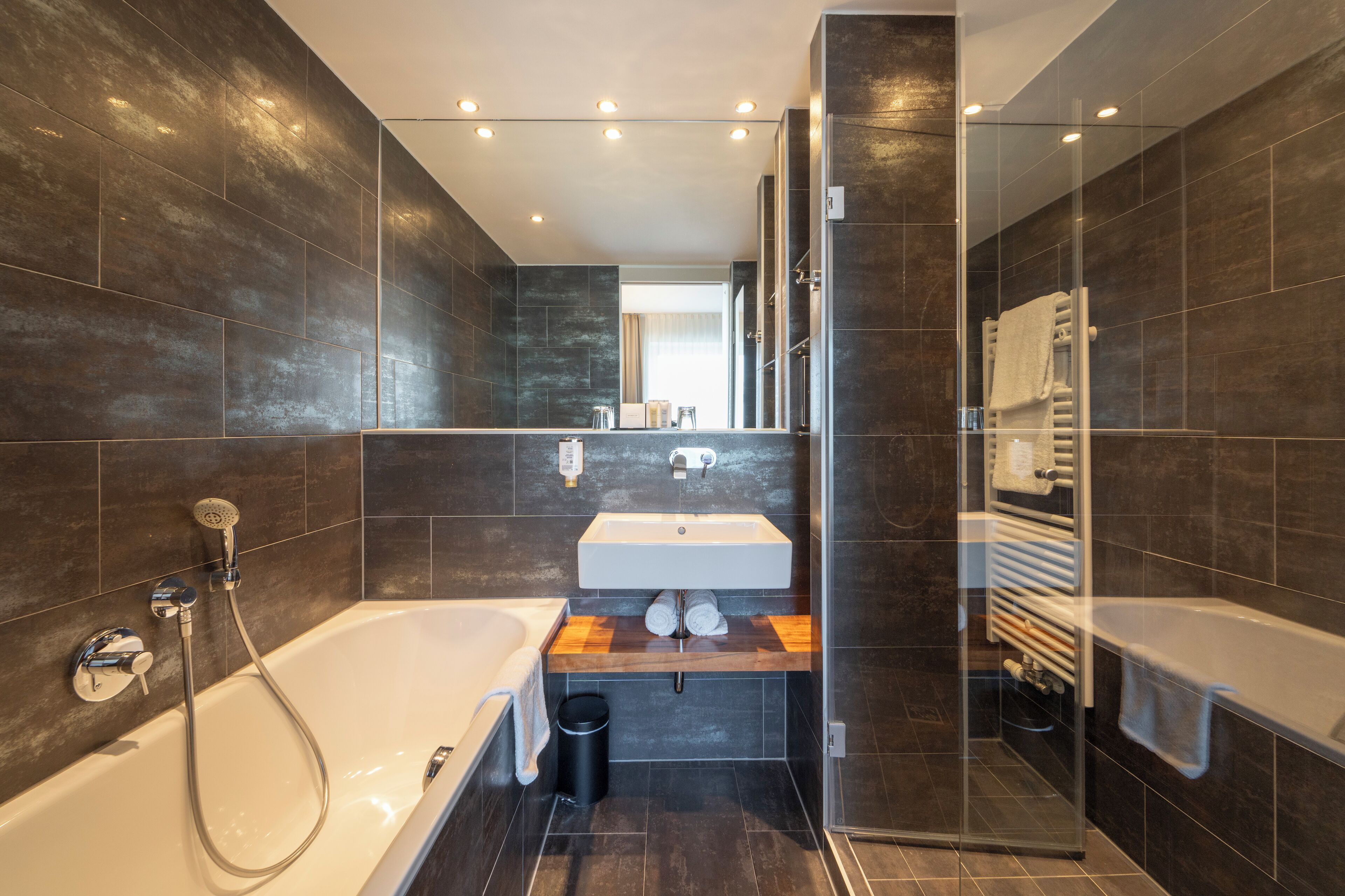 A modern bathroom with a large bathtub, a glass-enclosed shower, and a wooden vanity.