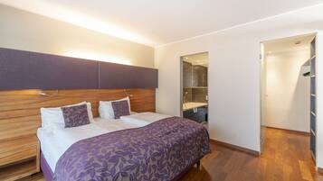 A modern bedroom with a wooden headboard, a large bed with a purple floral bedspread, a built-in bench, and a walk-in closet.