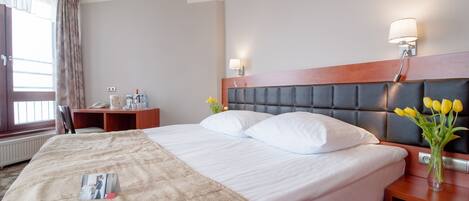 Una habitación de hotel con una cama grande, una mesita de noche con lámpara, un escritorio con silla y una ventana con cortinas.