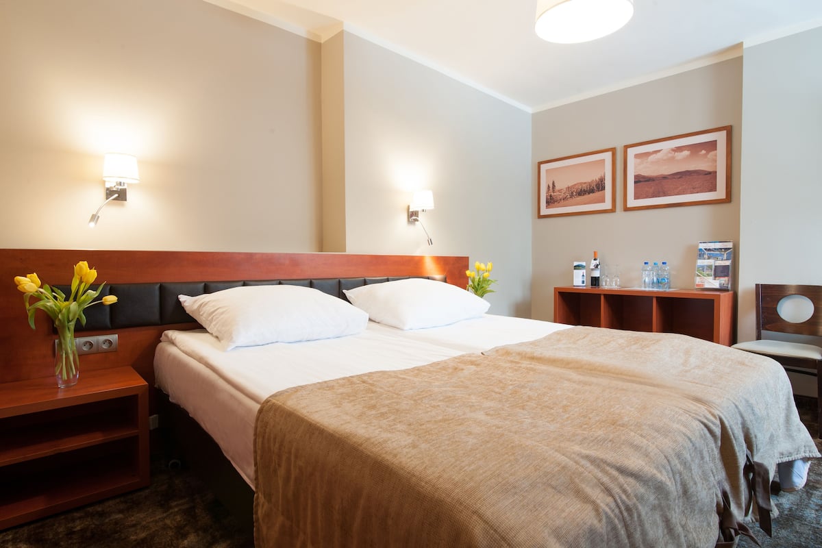 A hotel room with a large bed, two bedside tables, a nightstand, a desk, and two wall-mounted lamps.