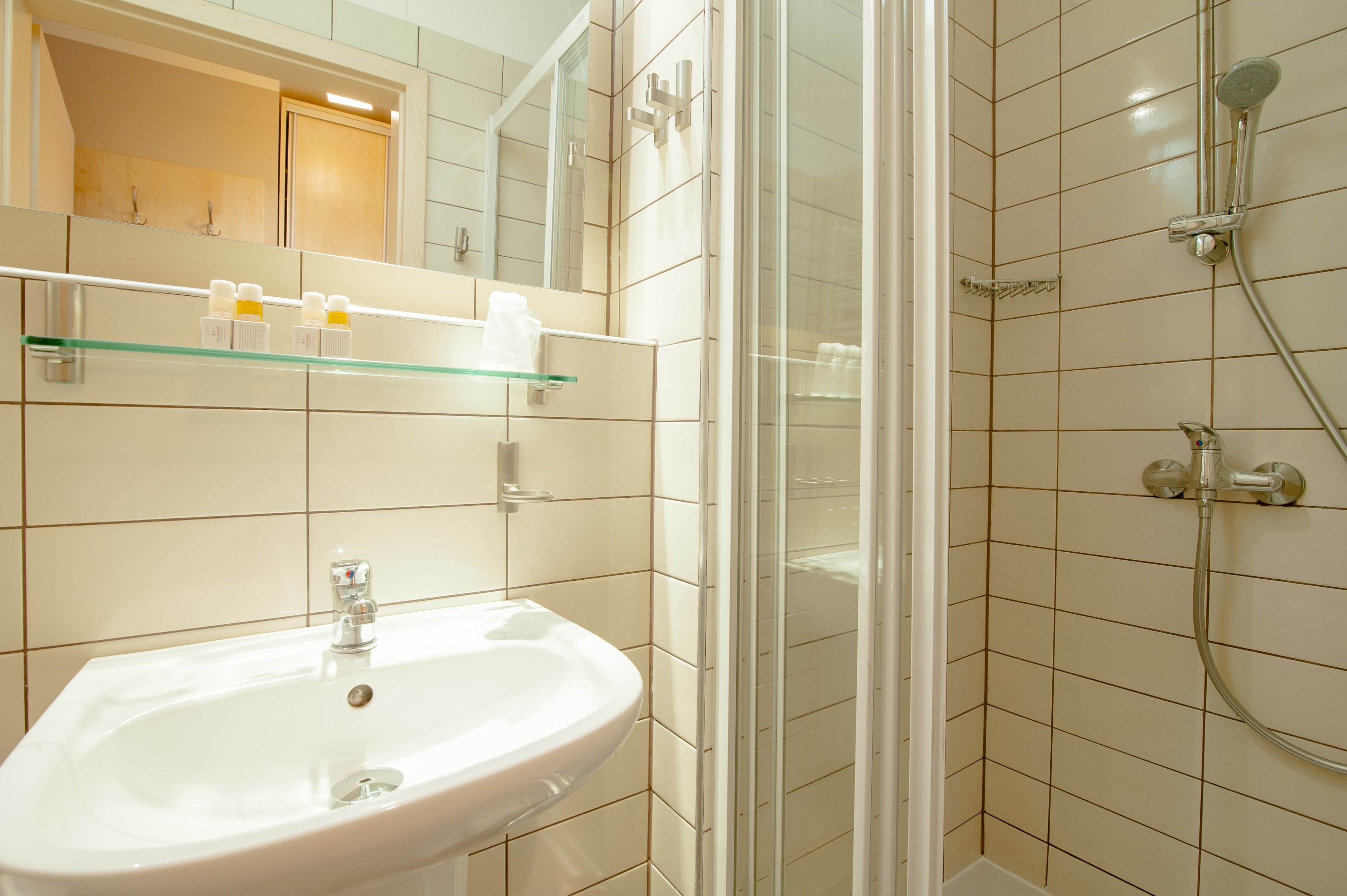 A bathroom with a sink, glass shelf, and shower area.