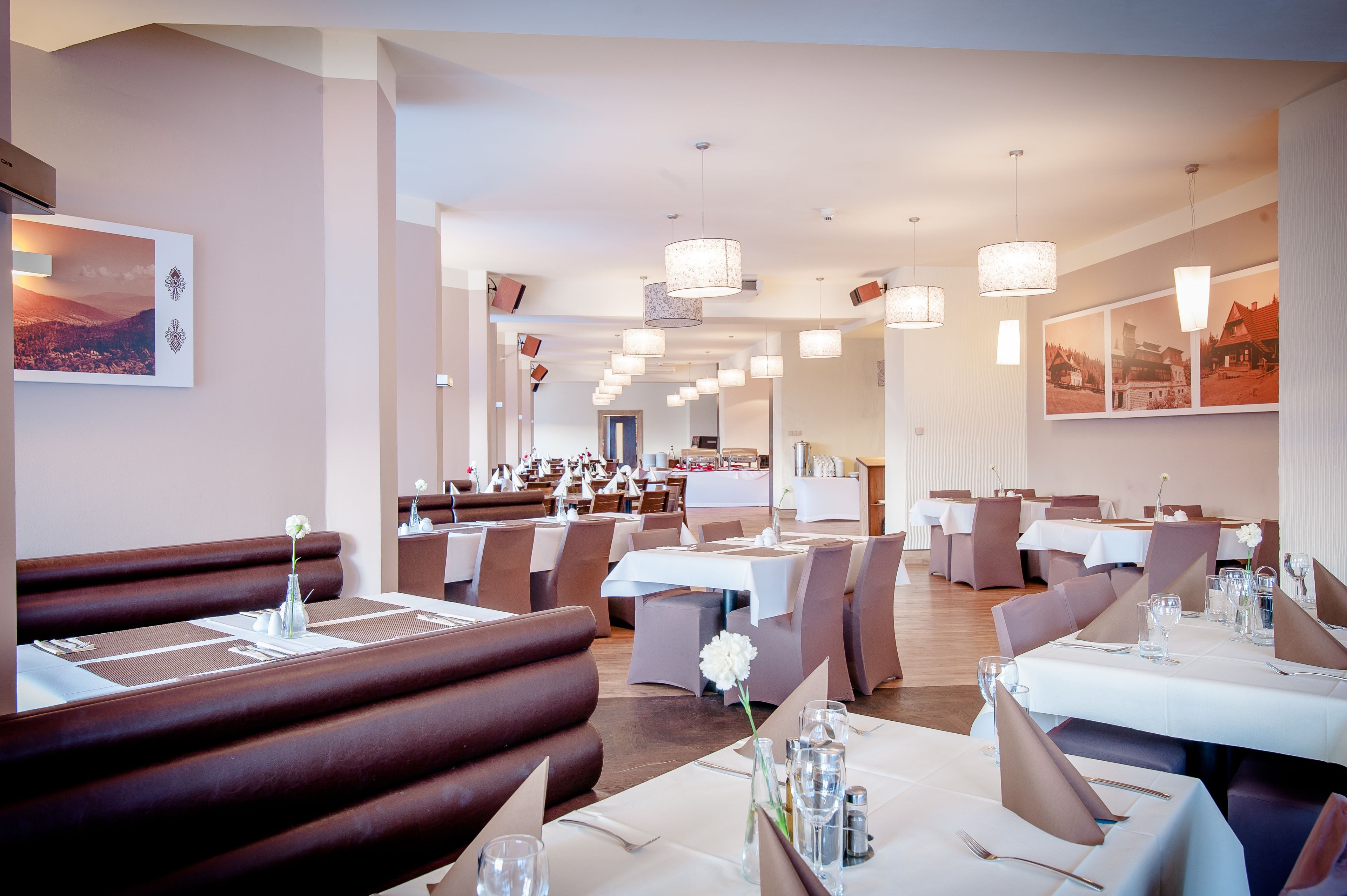 Ein Restaurant mit Sitzecken und Tischen, alle mit weißen Tischdecken und Besteck gedeckt.
