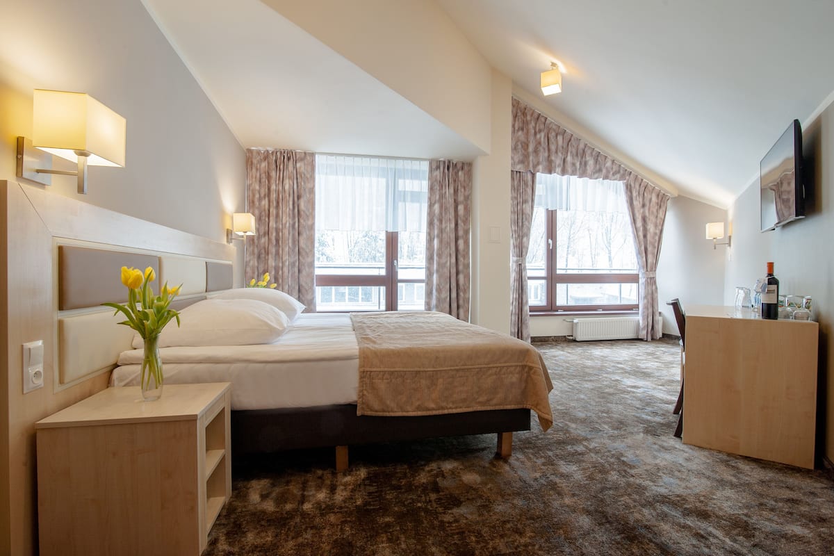 A bedroom with a bed, bedside tables, a dresser, a TV, and large windows with curtains.