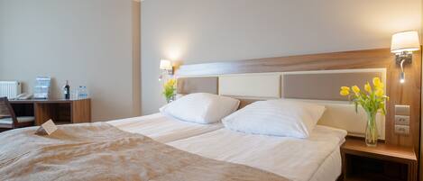 A hotel room with two beds, a desk, and a nightstand with lamps.
