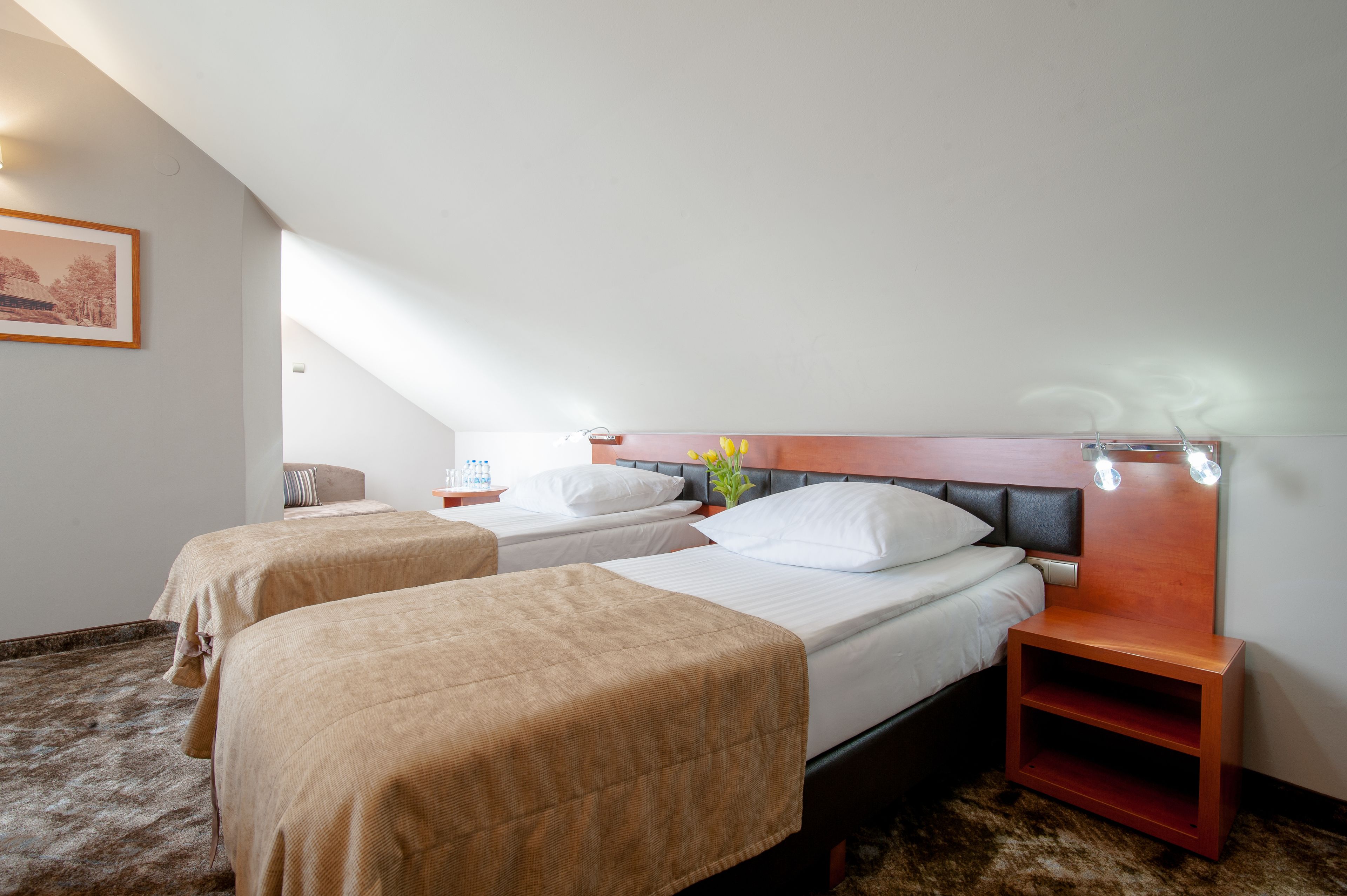 A hotel room with two beds, a nightstand, a small shelf, and a framed picture on the wall.