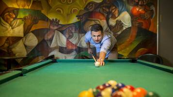 A person playing pool in a room with a large, colorful mural on the wall.