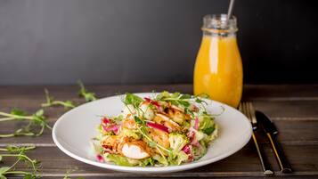 A plate of salad with chicken and vegetables, a glass of orange juice, and a fork and knife on a wooden table.