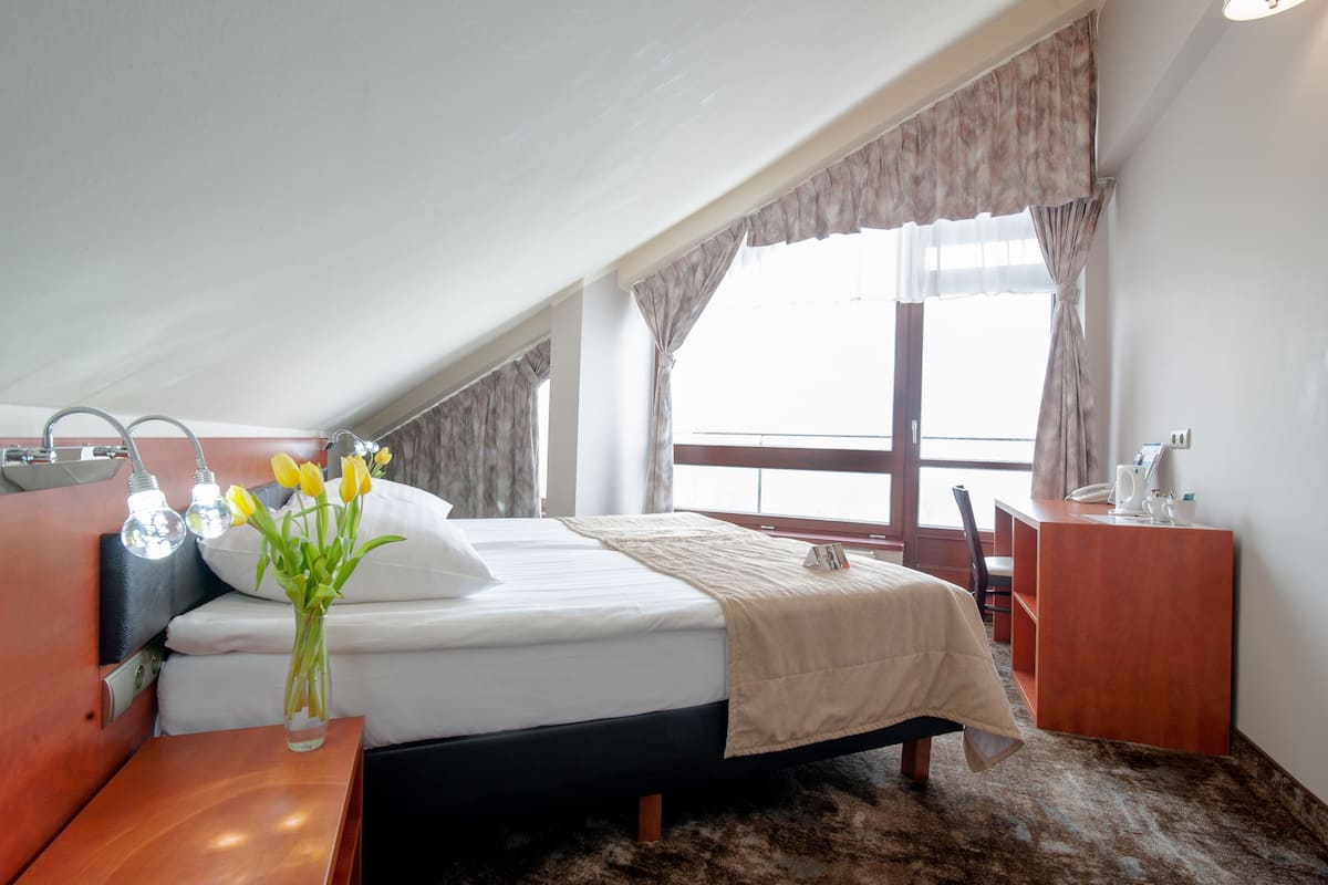 A hotel room with a bed, bedside table, lamp, and a window with curtains.