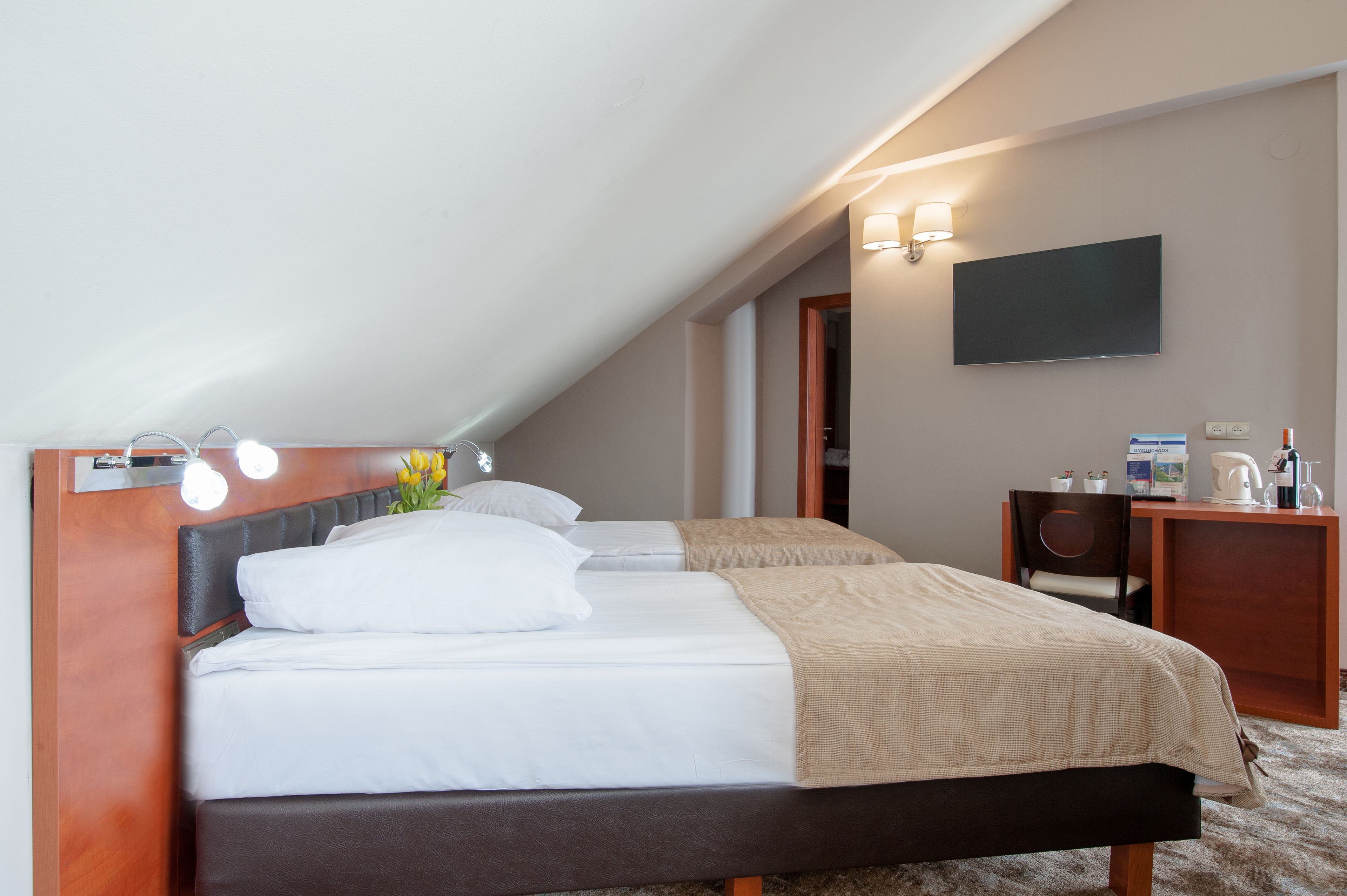 A hotel room with two beds, a desk, a flat-screen TV, and a small kitchenette.