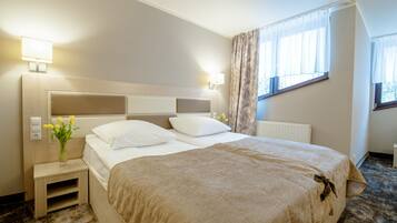 A hotel room with a large bed, bedside lamps, a nightstand, a window with curtains, and a radiator.