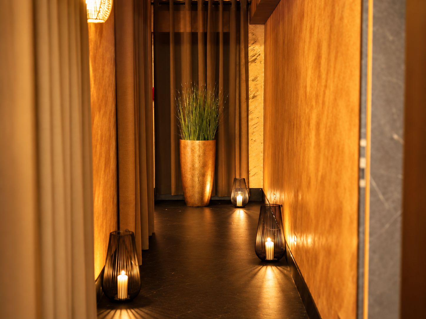 A hallway with wooden walls, a potted plant, and two lit candles.