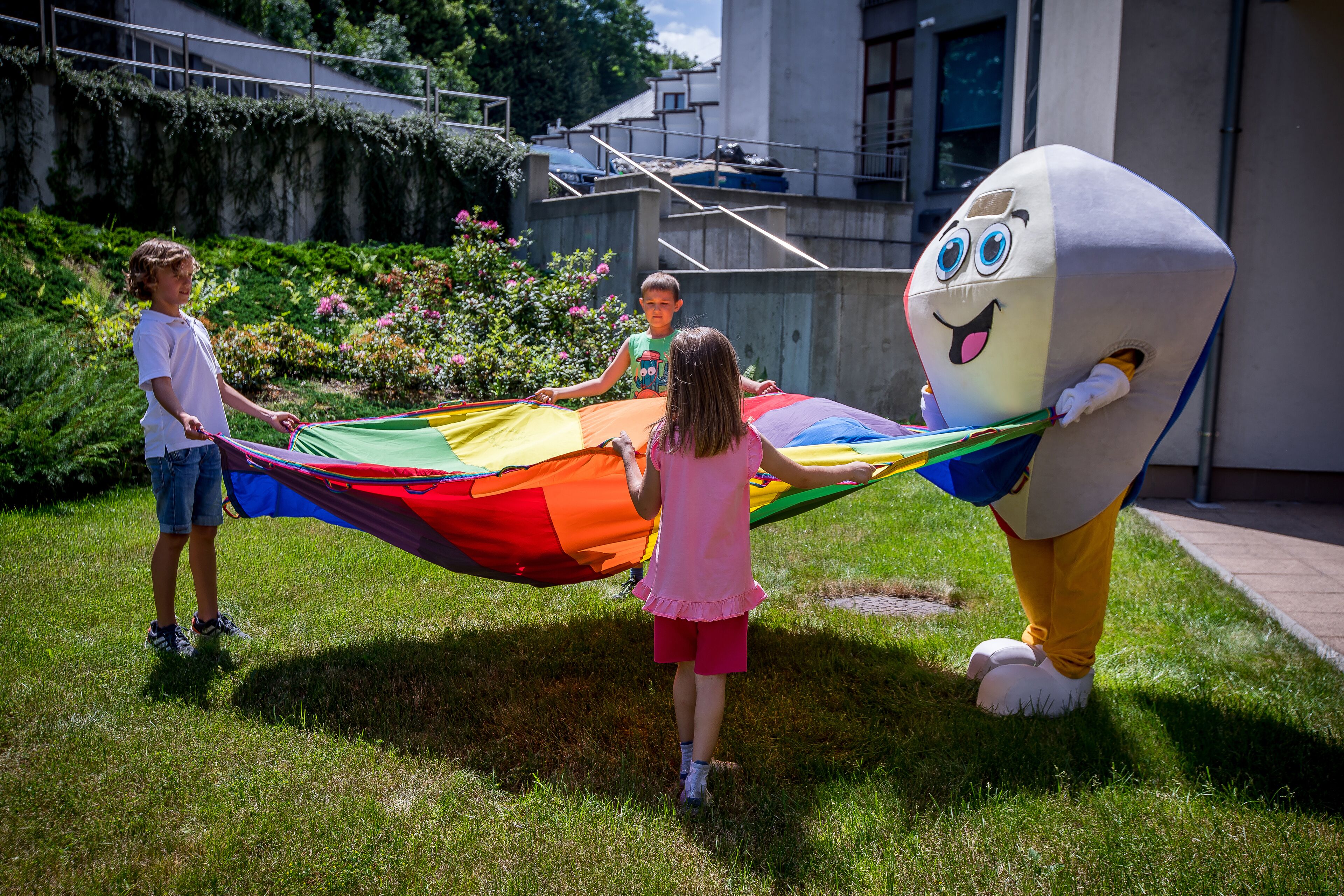 A grassy area with a large, colorful kite being held by a person and a mascot.