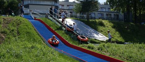 A water slide with inflatable tubes, surrounded by greenery and a building with a sign reading "HOTEL DIAMANT".