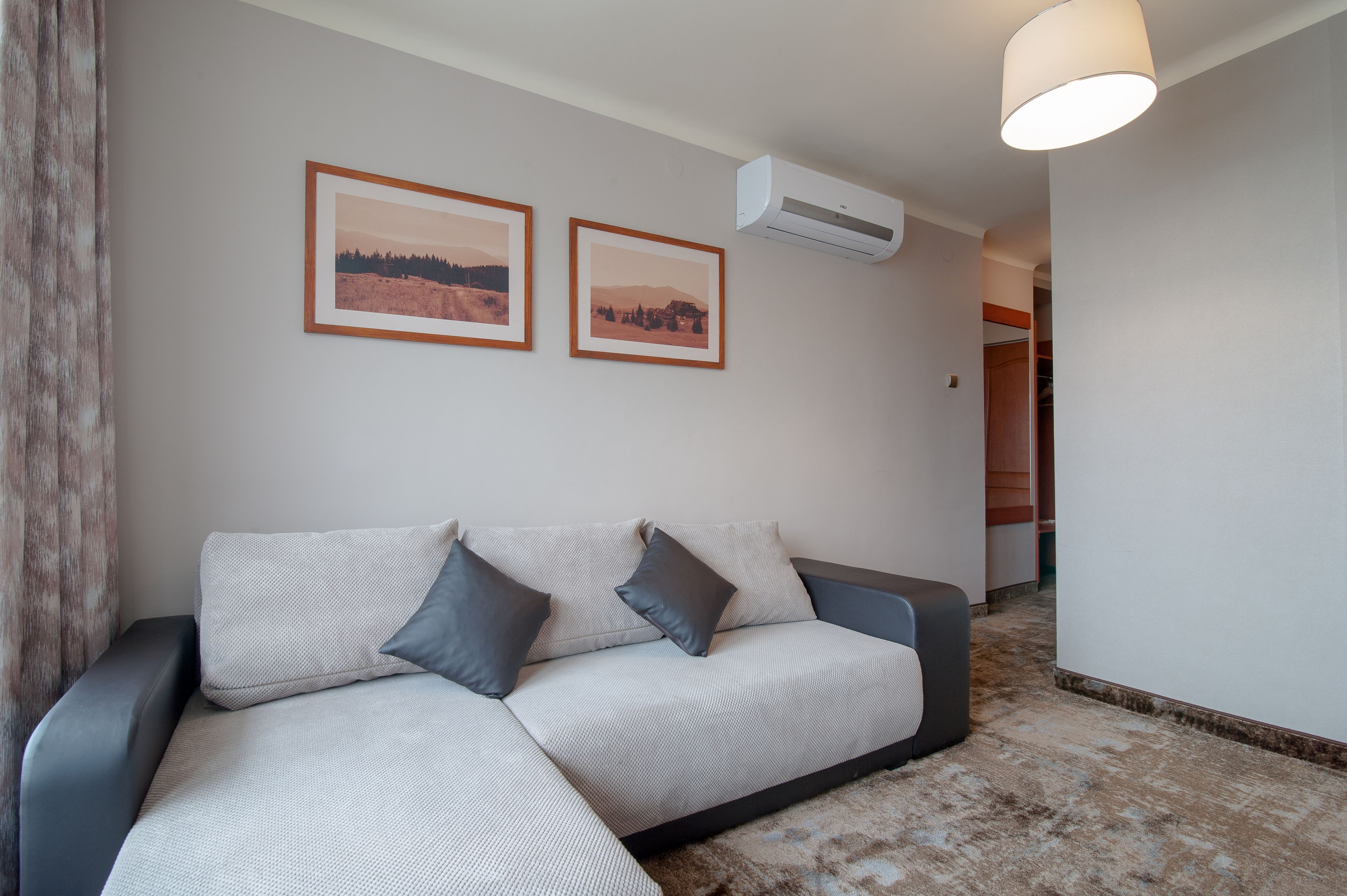 A modern living room with a sofa, two framed pictures on the wall, and an air conditioning unit.