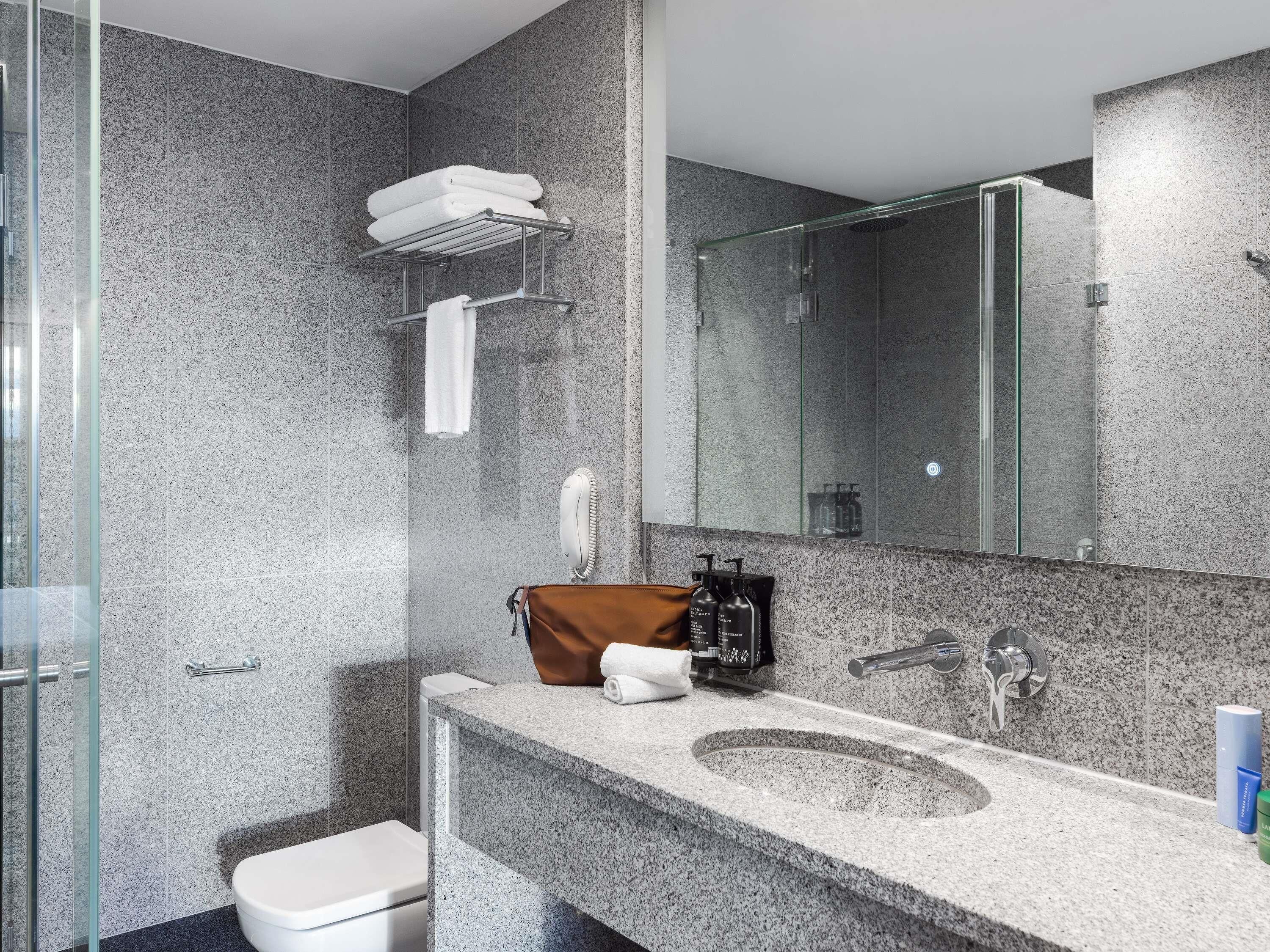 Une salle de bain moderne avec des comptoirs en granit, une cabine de douche en verre et un grand miroir.