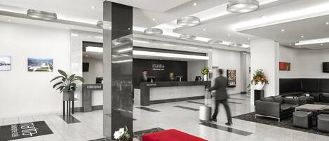 A modern hotel lobby with a reception desk, seating area, and a large window.