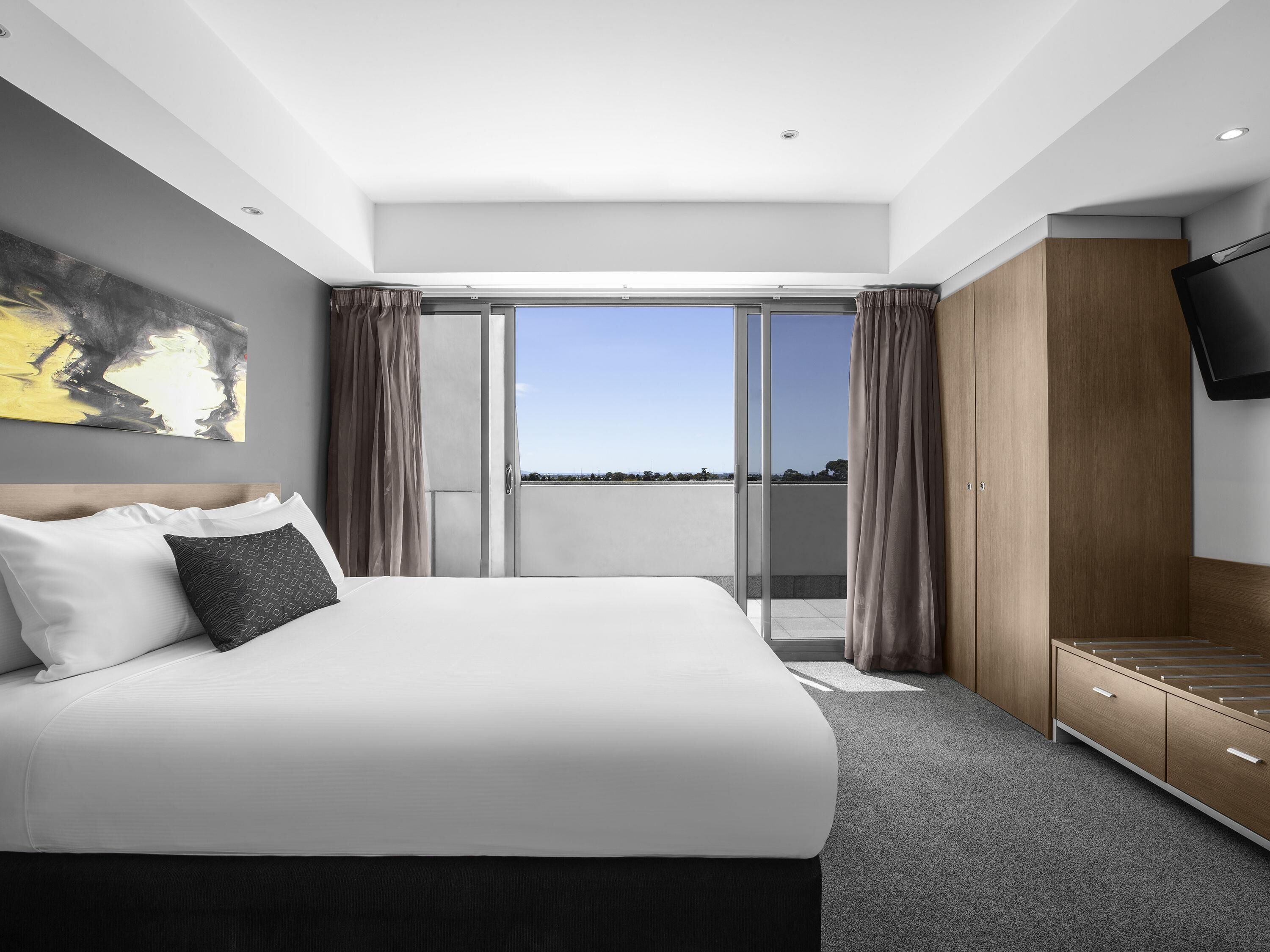 A modern hotel room with a large bed, a TV, a wardrobe, and a balcony with a city view.