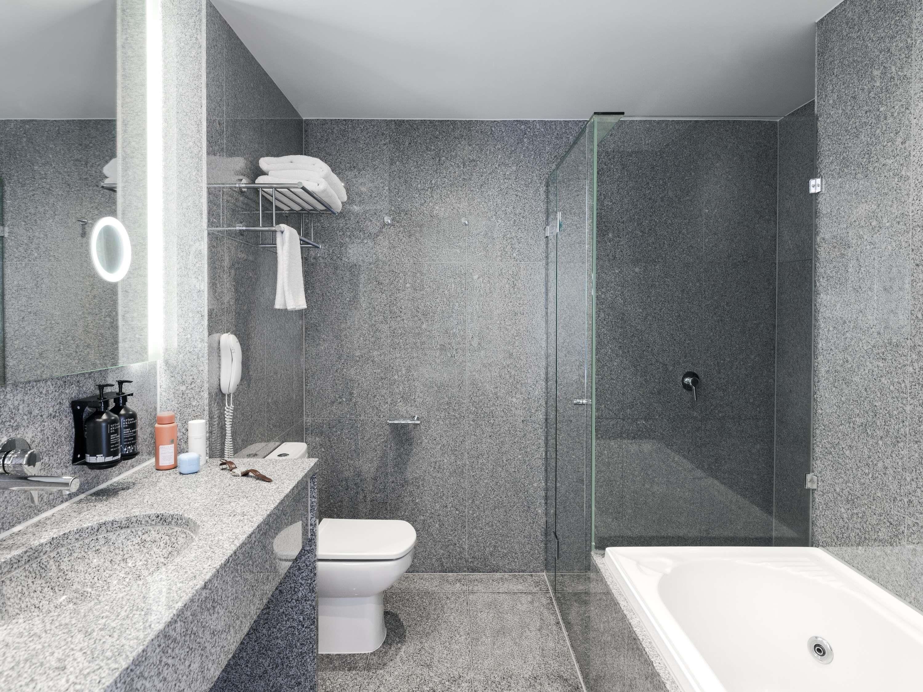 A modern bathroom with a granite countertop, a white toilet, a glass-enclosed shower, and a large bathtub.