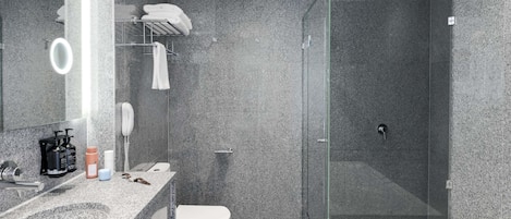 Un baño moderno con encimera de granito, inodoro blanco, ducha con mampara de vidrio y una bañera grande.
