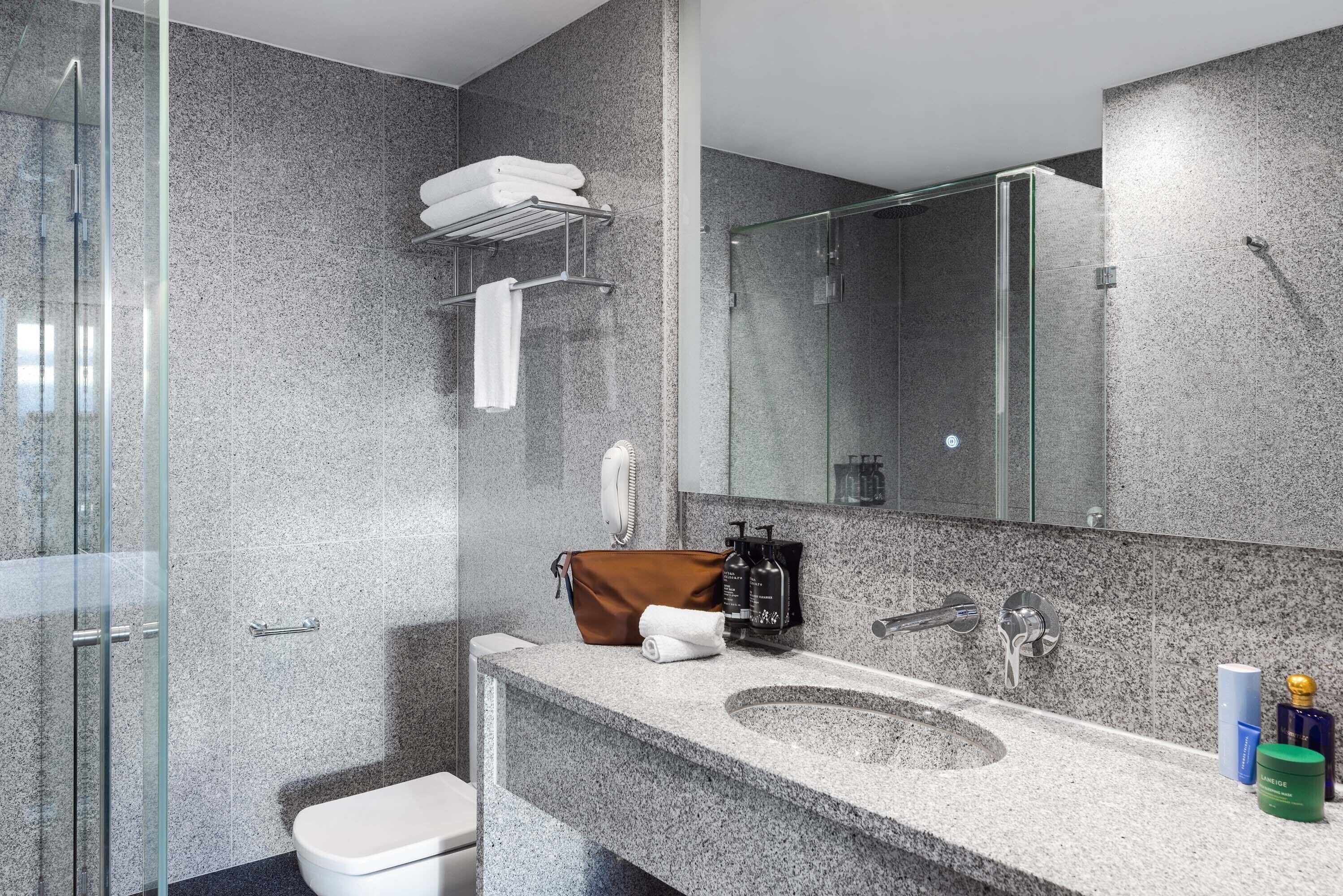 Un bagno moderno con un piano di lavoro in granito, cabina doccia in vetro e un ampio specchio.