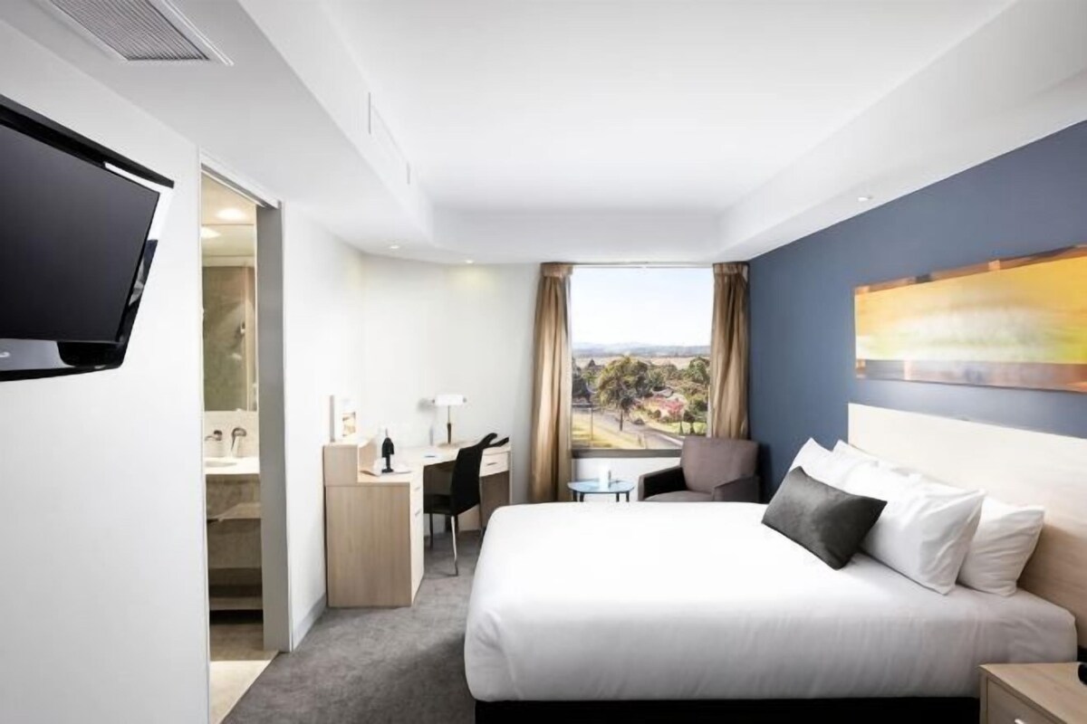 A hotel room with a bed, desk, chair, and a television.