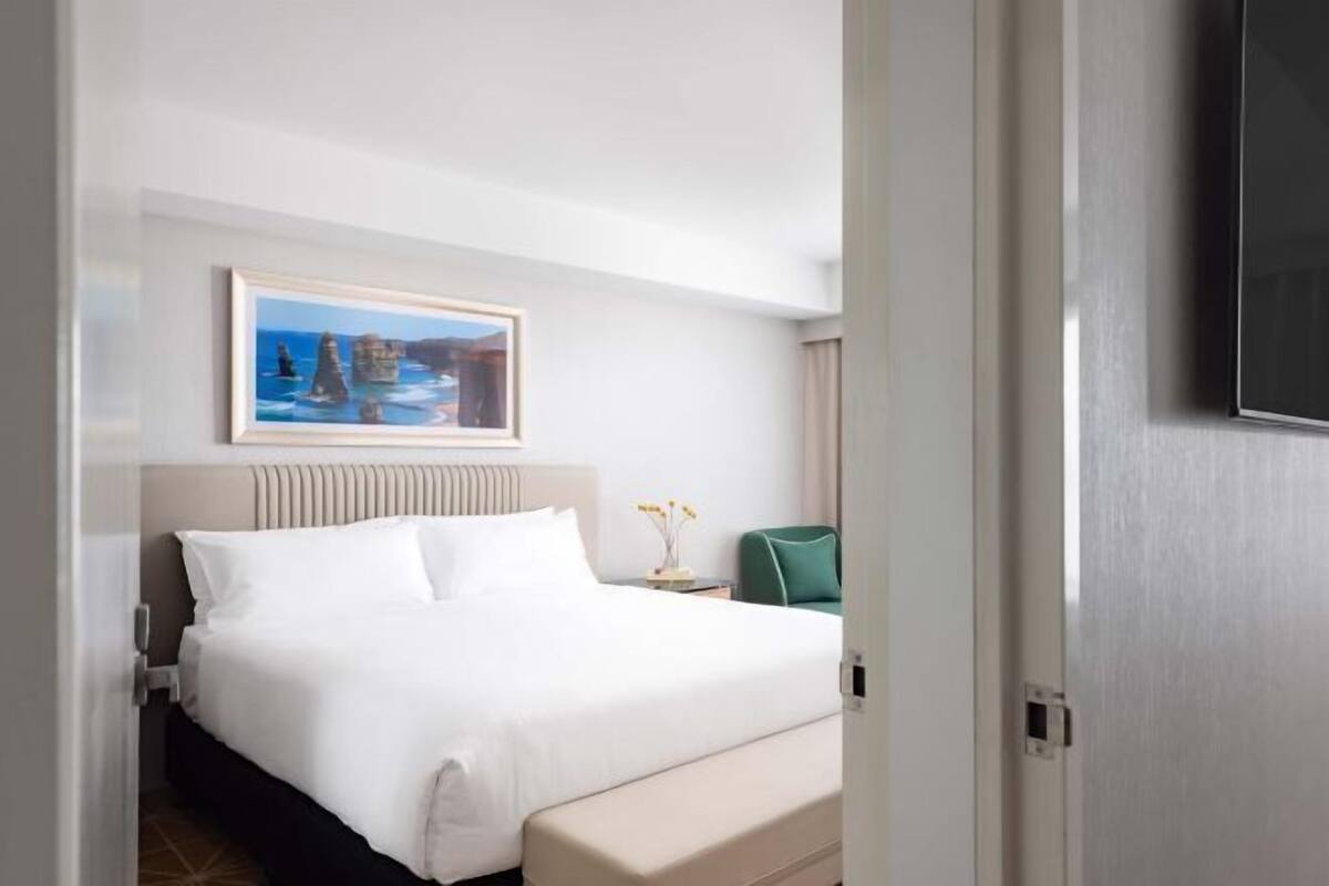 A hotel room with a bed, a painting, a nightstand, and a television.