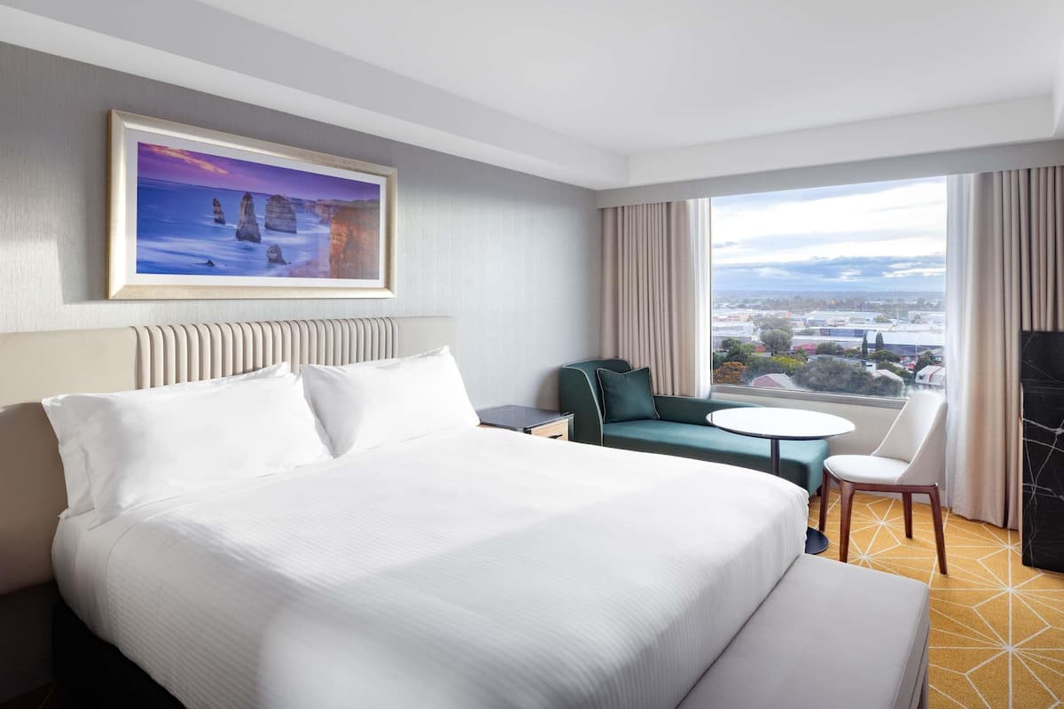 A hotel room with a large bed, a sofa, a small table, and a view of the city.