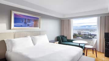 Quarto de hotel com uma cama grande, um sofá, uma mesinha e vista para a cidade.