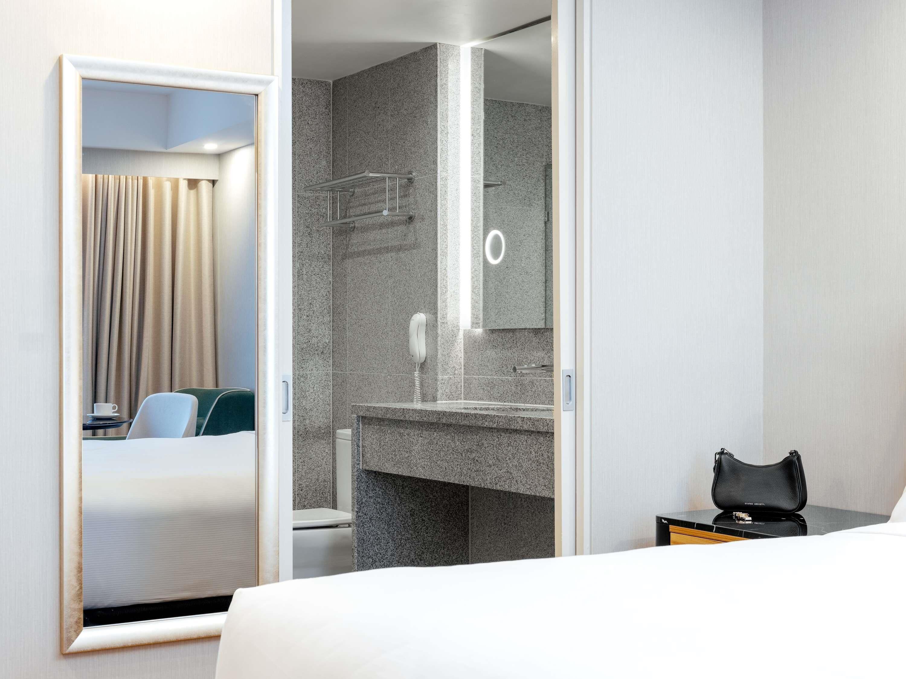 Ein Hotelzimmer mit Bett, Badezimmer mit Spiegel und einem kleinen Tisch mit einer Handtasche.