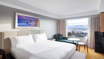 Un cuarto de hotel con una cama grande, un cuadro en la pared, un sofá, una mesita y vistas de la ciudad a través de la ventana.