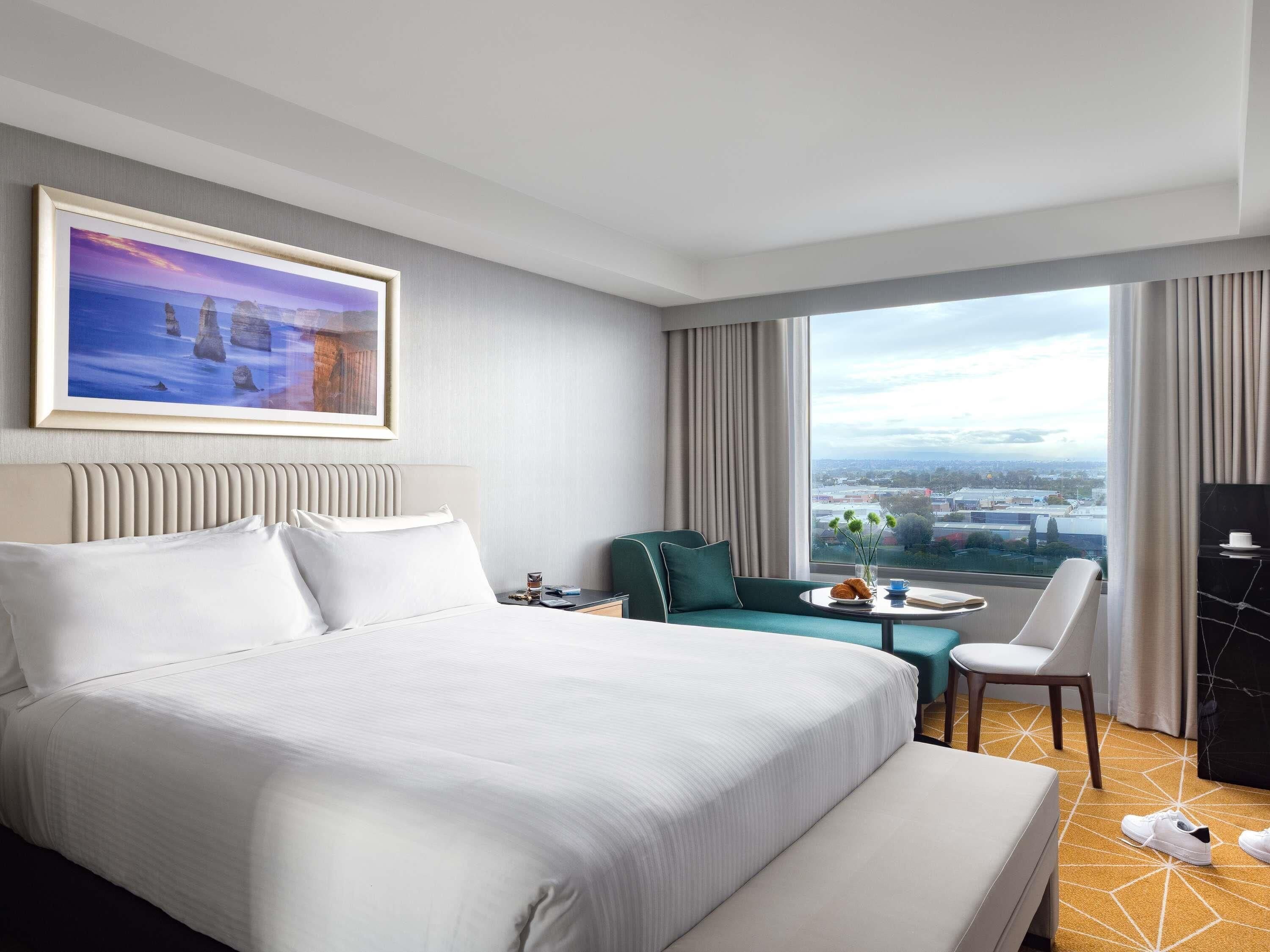 Une chambre d’hôtel avec un grand lit, une vue sur la ville, une table à manger et une chaise.