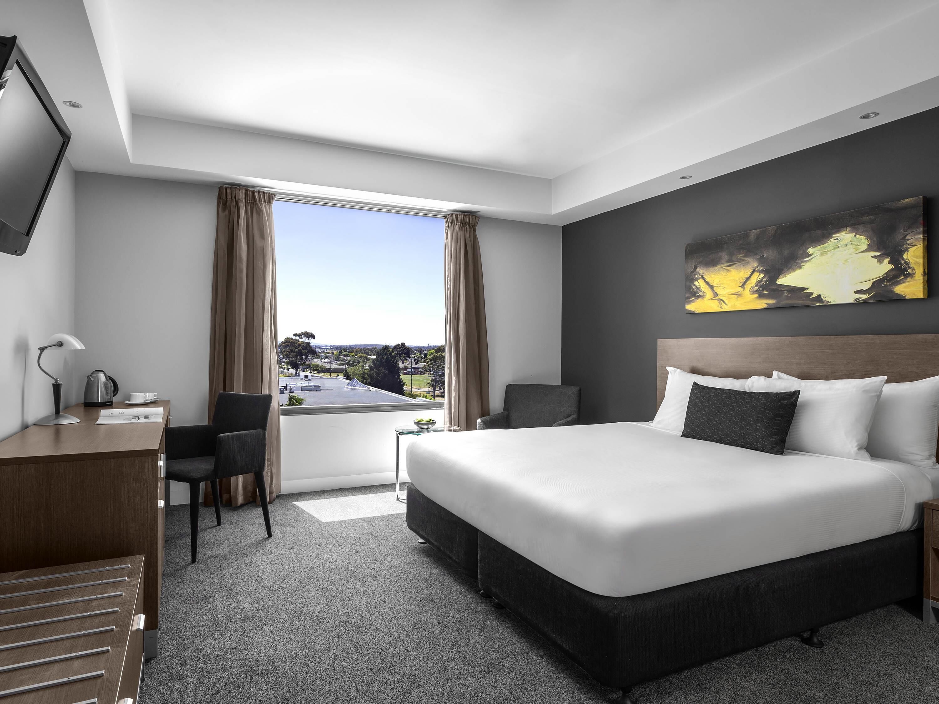 Ett modernt hotellrum med en stor säng, ett skrivbord, en stol och utsikt över staden.