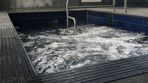 A hot tub with a metal ladder, surrounded by blue tiles and a concrete wall.