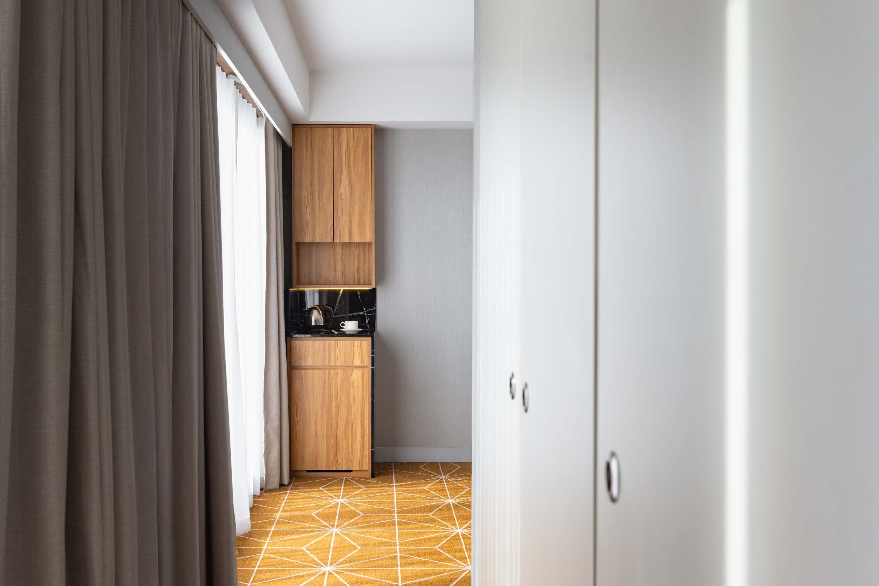 A narrow hallway with a geometric patterned floor, wooden cabinets, and a coffee maker on a counter.