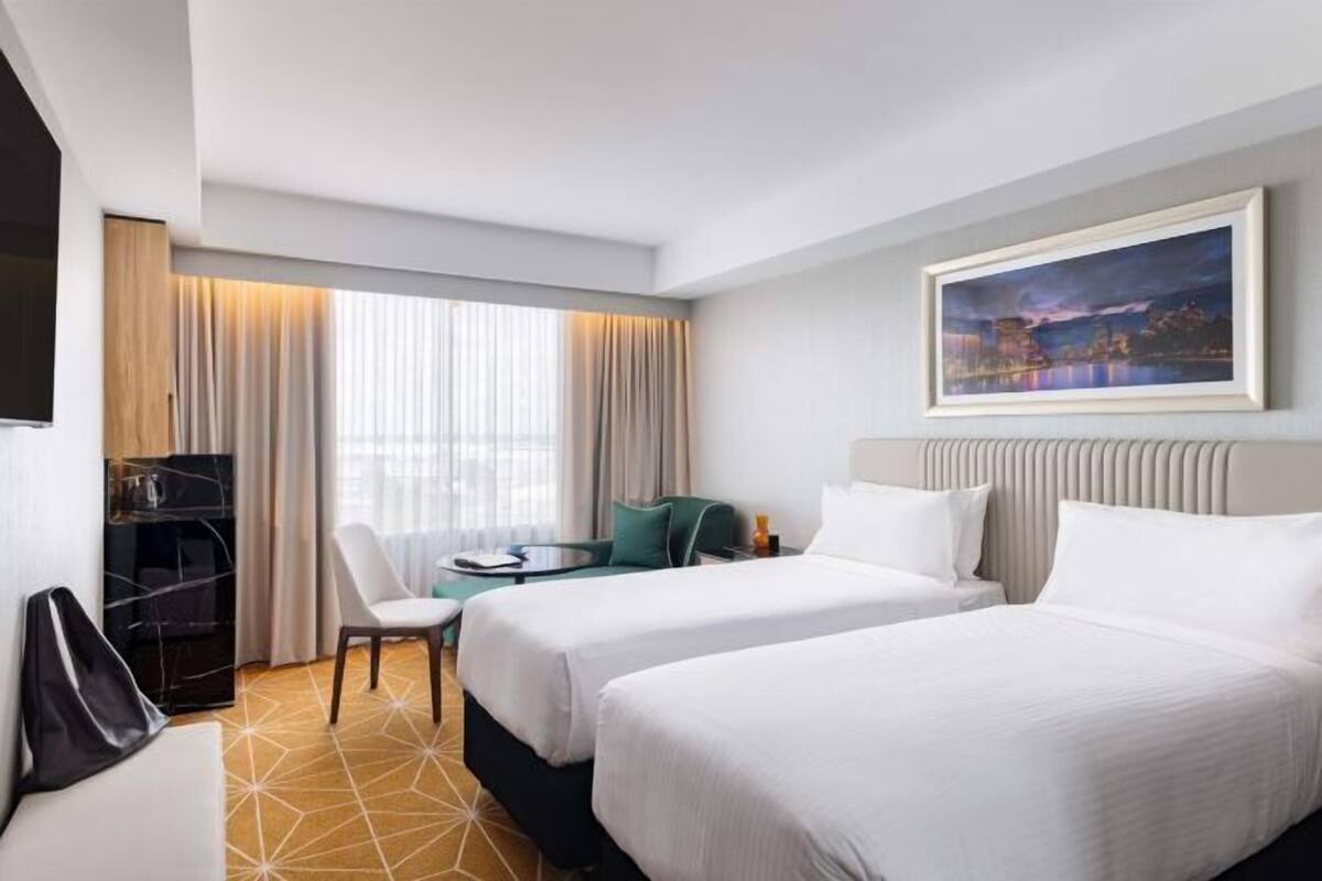 A hotel room with two beds, a desk, a chair, a TV, and a painting on the wall.