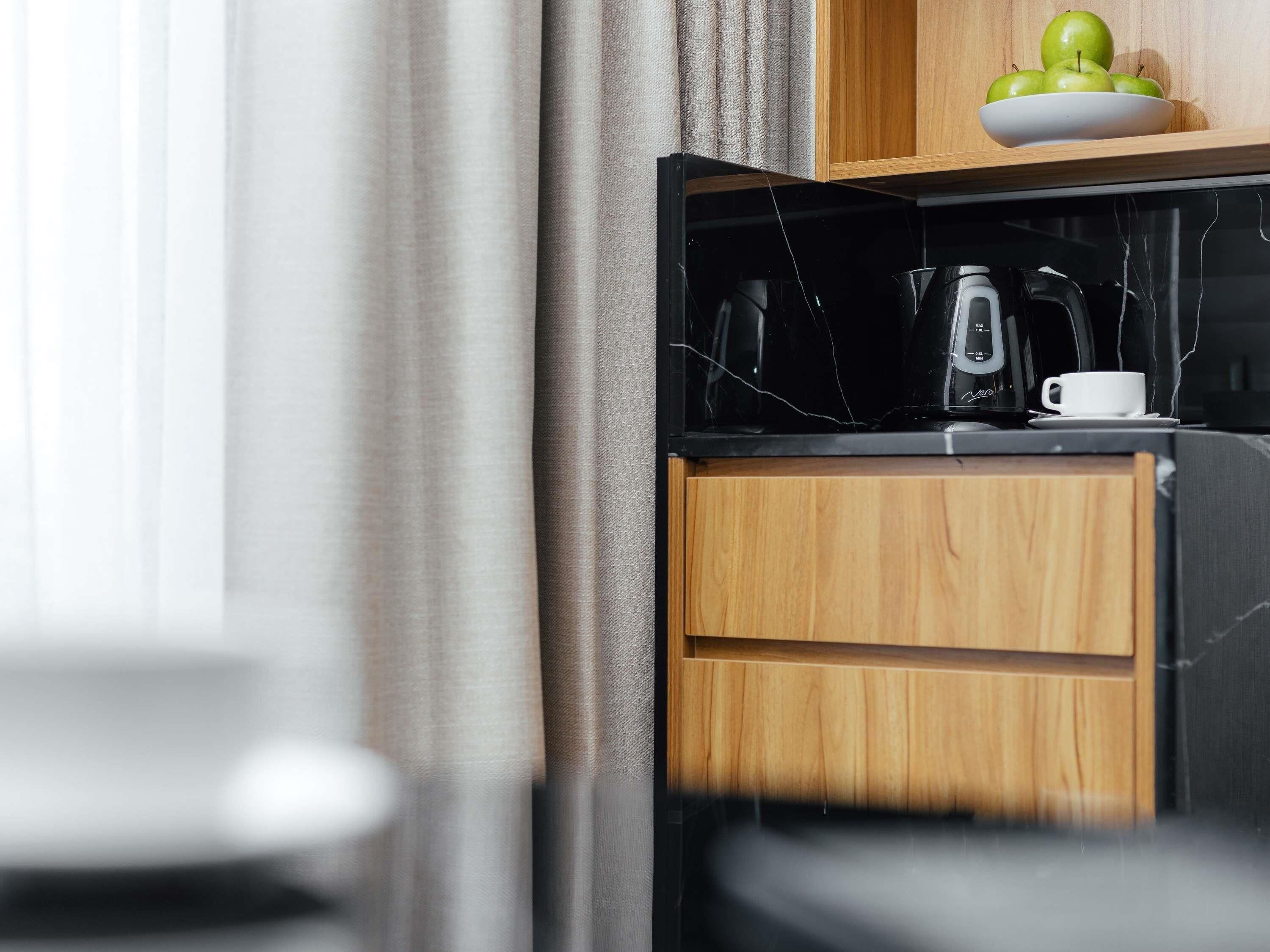 Una cocina moderna con encimera de mármol negro, una cafetera y un bol con manzanas sobre un estante de madera.