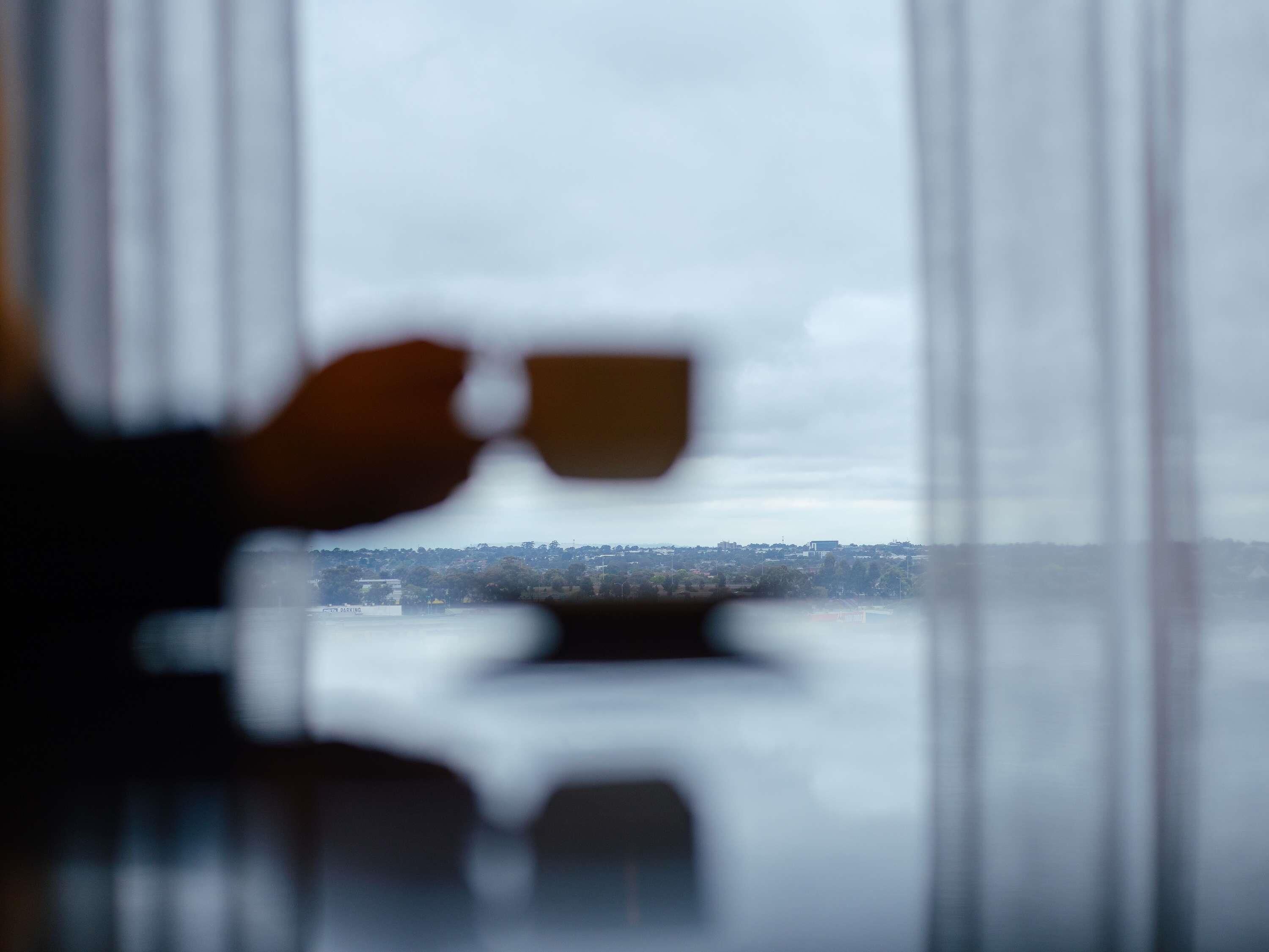 A blurred view through a window with a hand holding a cup, and a distant cityscape.