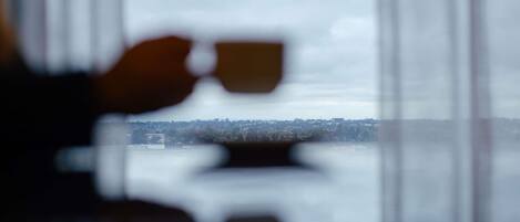 A blurred view through a window with a hand holding a cup, and a distant cityscape.