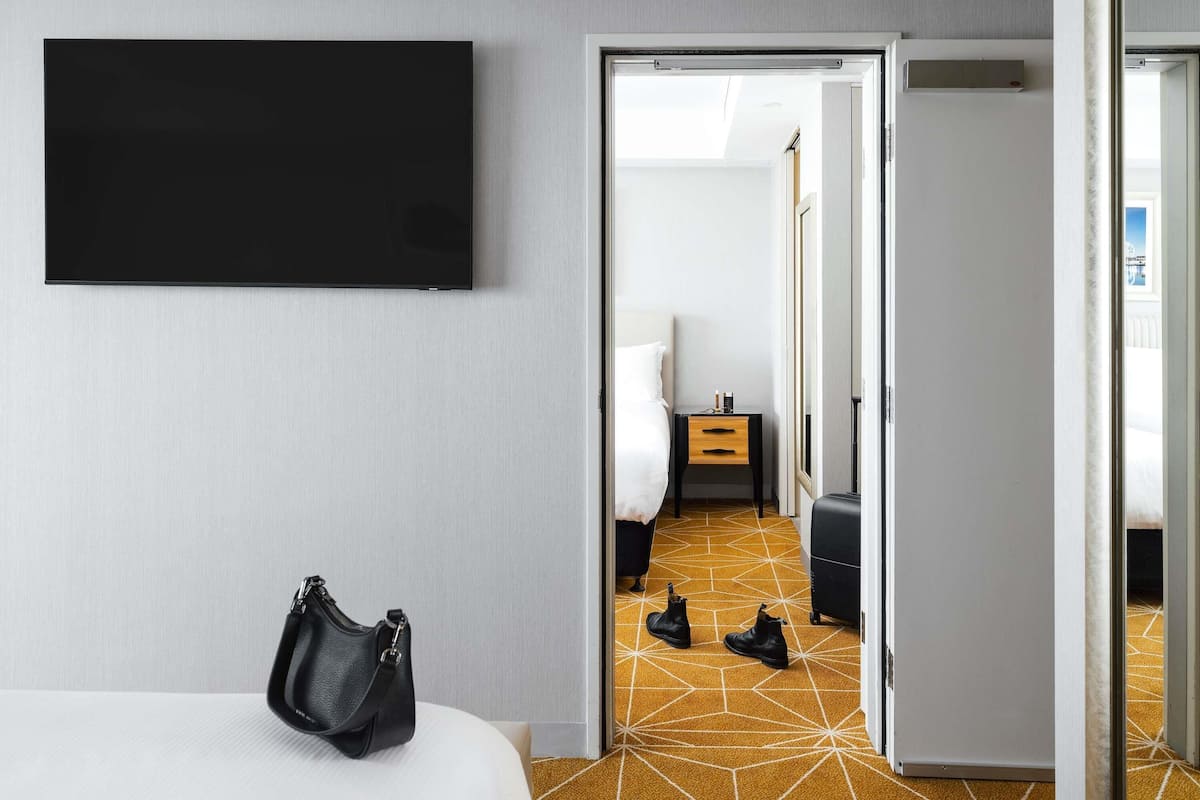 A hotel room with a bed, a TV, a wardrobe, and a door leading to another room.