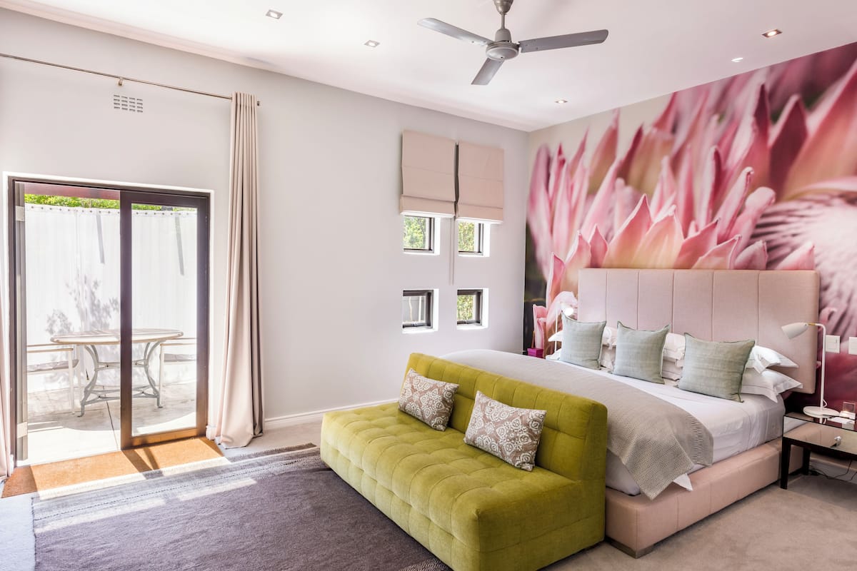 A bedroom with a bed, a green sofa, a ceiling fan, and a large window with curtains.