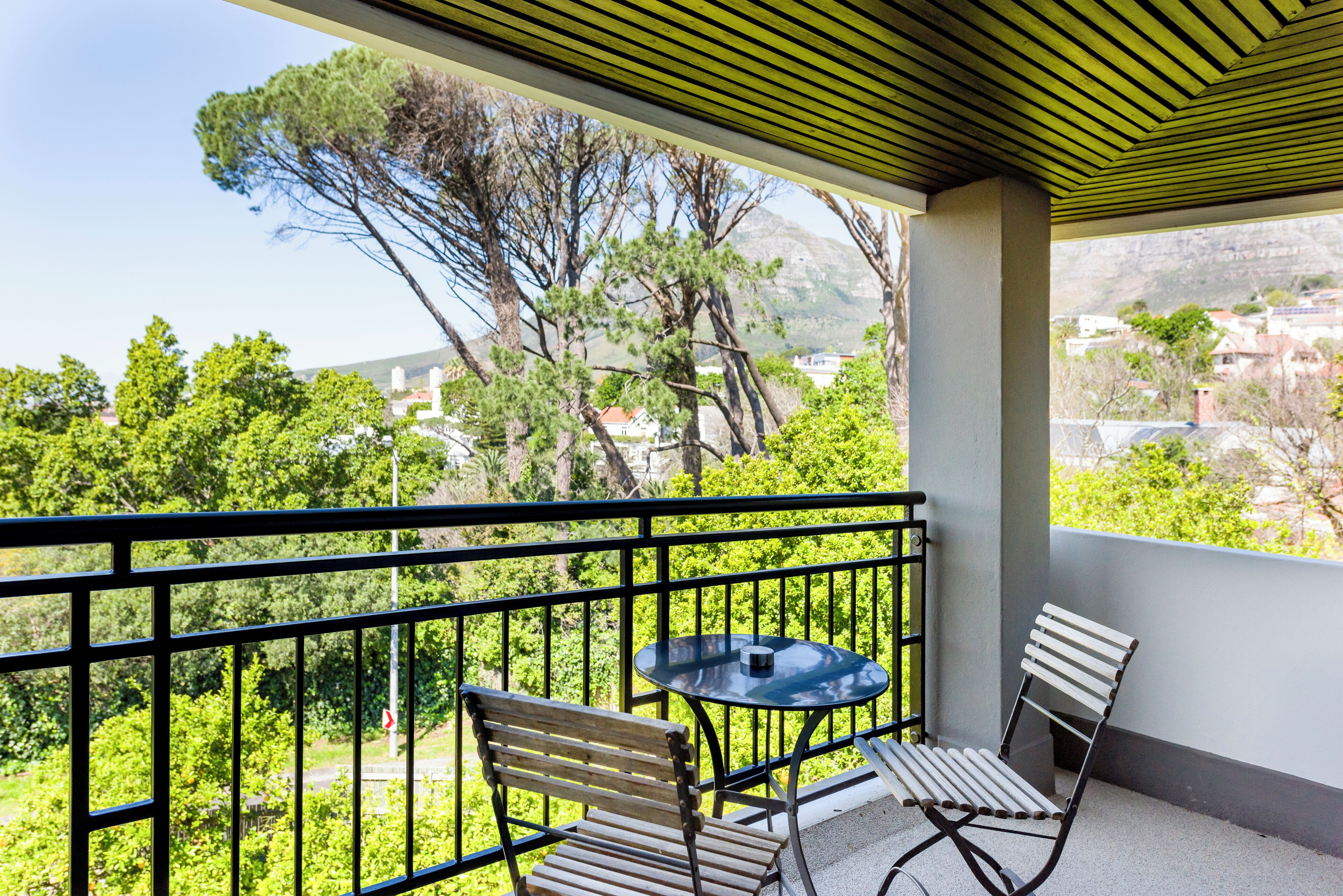 Un balcón con una mesa y dos sillas, con vistas a un paisaje verde con árboles y edificios.
