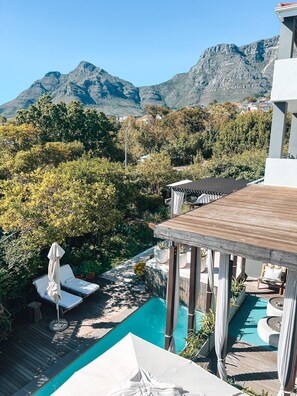A pool area with lounge chairs and a pergola, surrounded by lush greenery and mountains in the background. - Kensington Place (Cape Town)