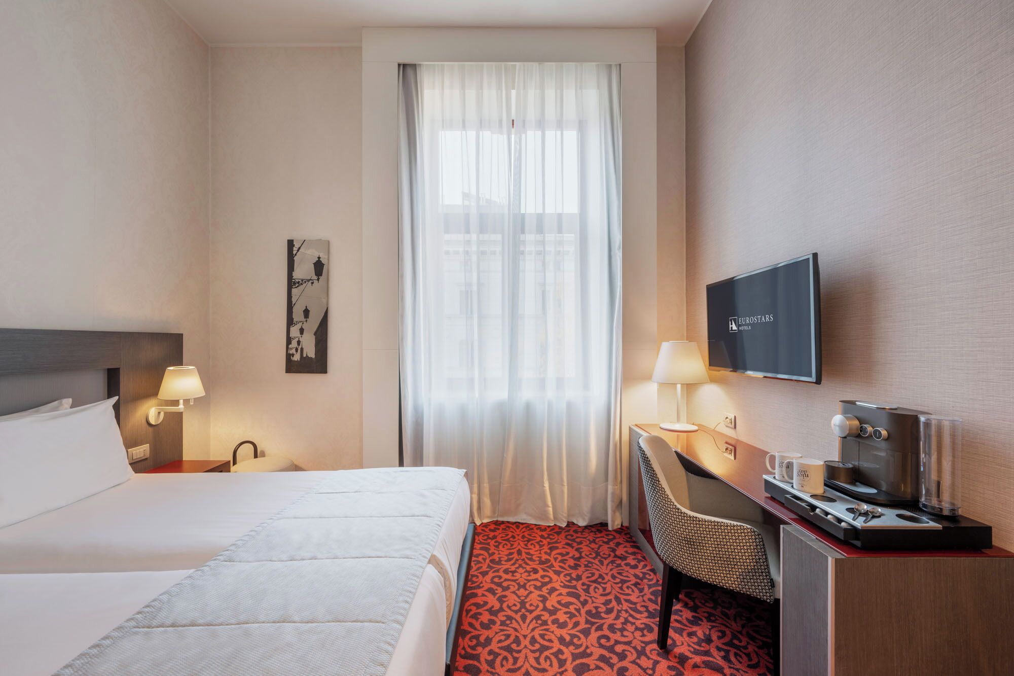 Una habitación de hotel con cama, escritorio con televisor, cafetera y silla.